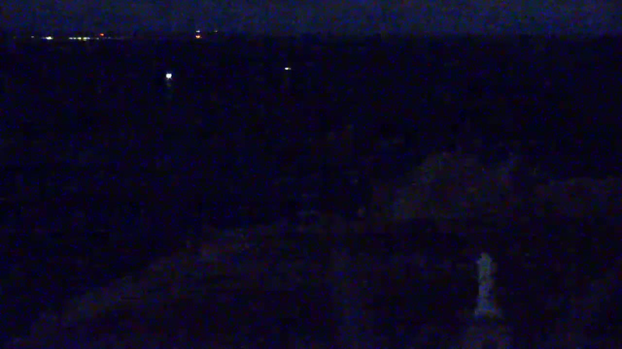 A dark, nighttime landscape is visible with a few distant lights, possibly from buildings or ships, and a faint glow near the bottom.