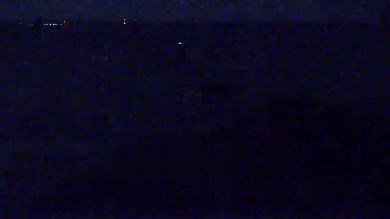 A dark, nighttime scene shows a blurry, indistinct landscape with a few faint lights visible in the distance.
