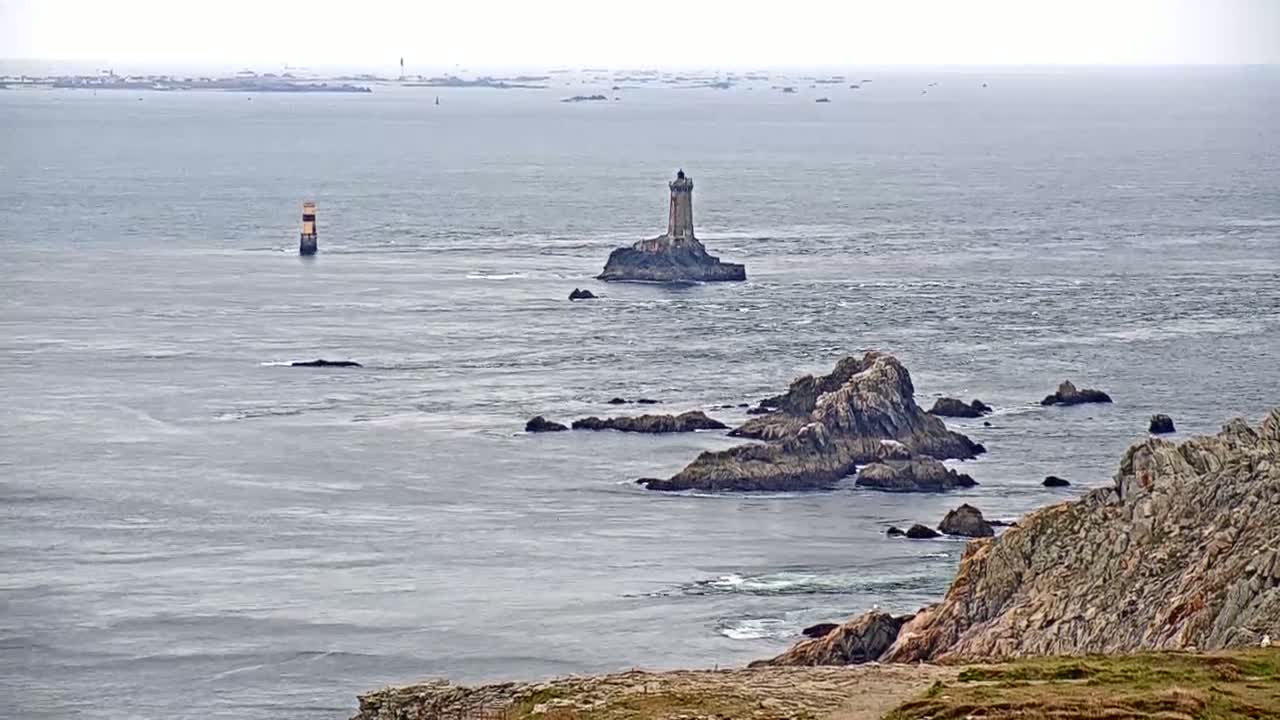 A rocky coastline with two lighthouses visible in the distance on a cloudy day, with a calm ocean.
