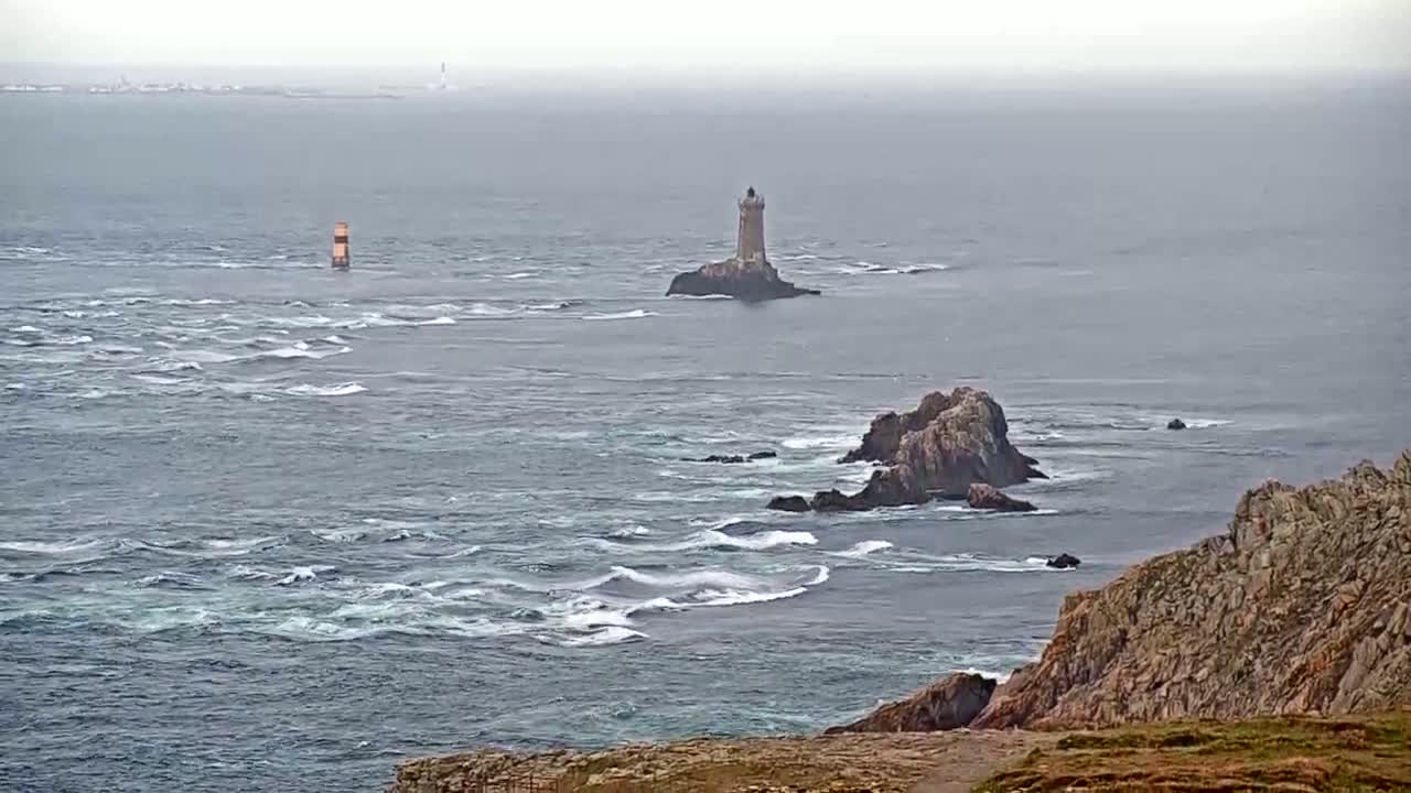 A rocky coast with a lighthouse on a small island in a choppy sea under an overcast sky.
