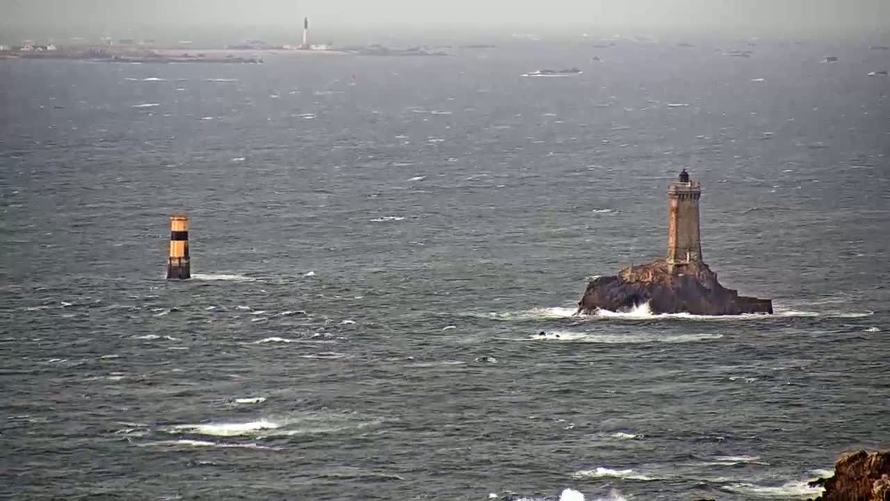 Two lighthouses stand in a choppy sea under an overcast sky, with a distant landmass visible in the background.