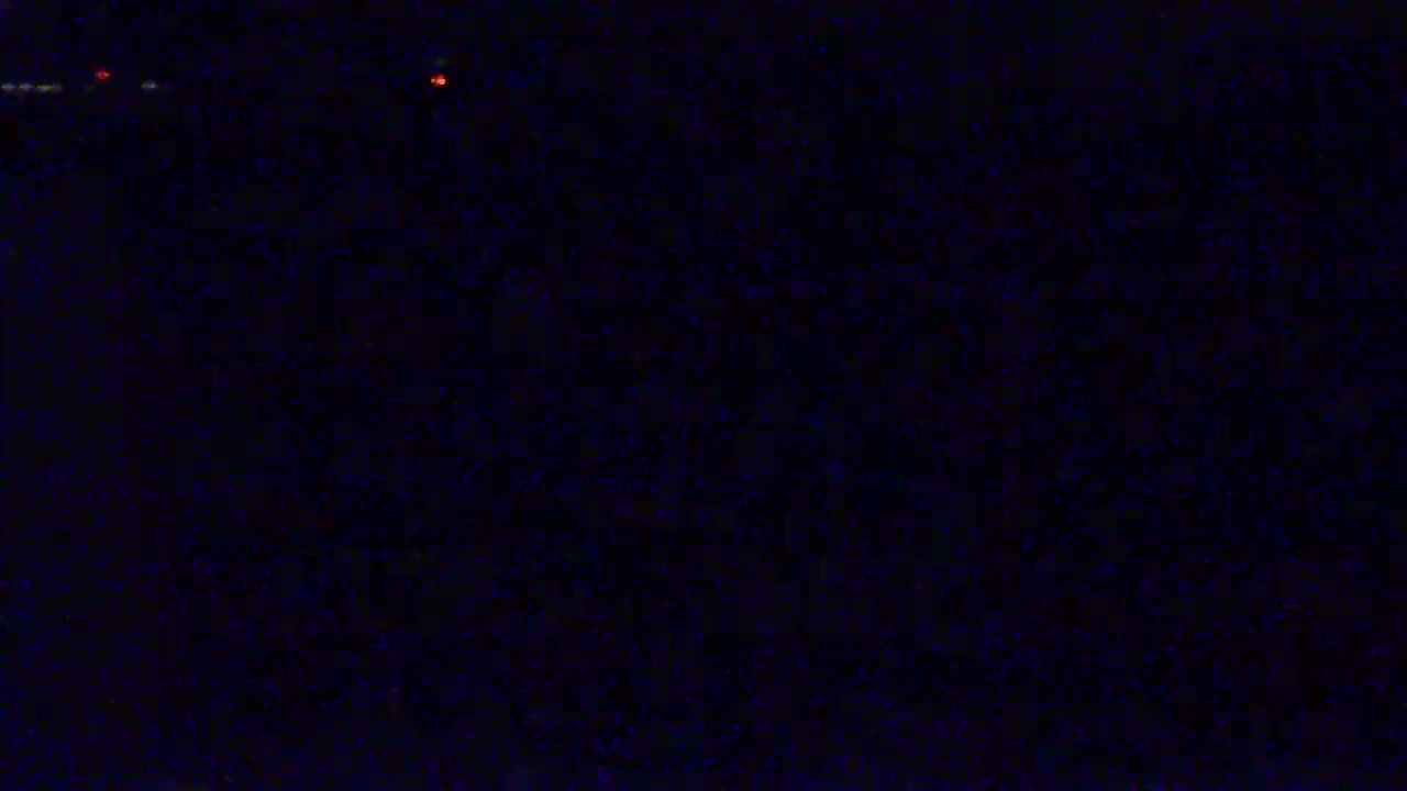 A dark, grainy image shows a few faint, distant red and white lights at night.