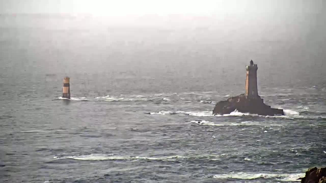 Two lighthouses stand in a choppy sea under a foggy sky.