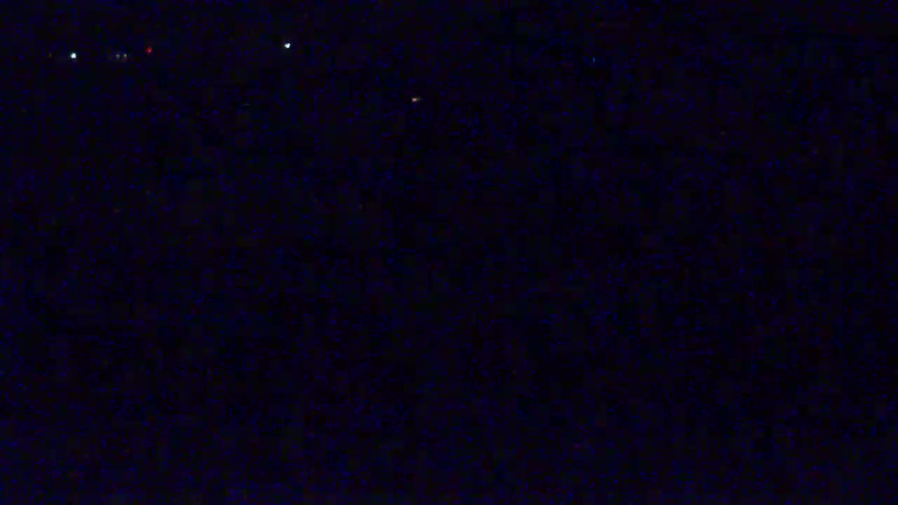 A dark, nighttime scene with a few faint lights visible in the distance.