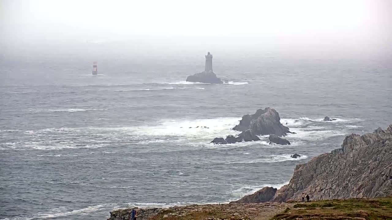 A foggy, wavy ocean with two lighthouses and rocky coastlines.