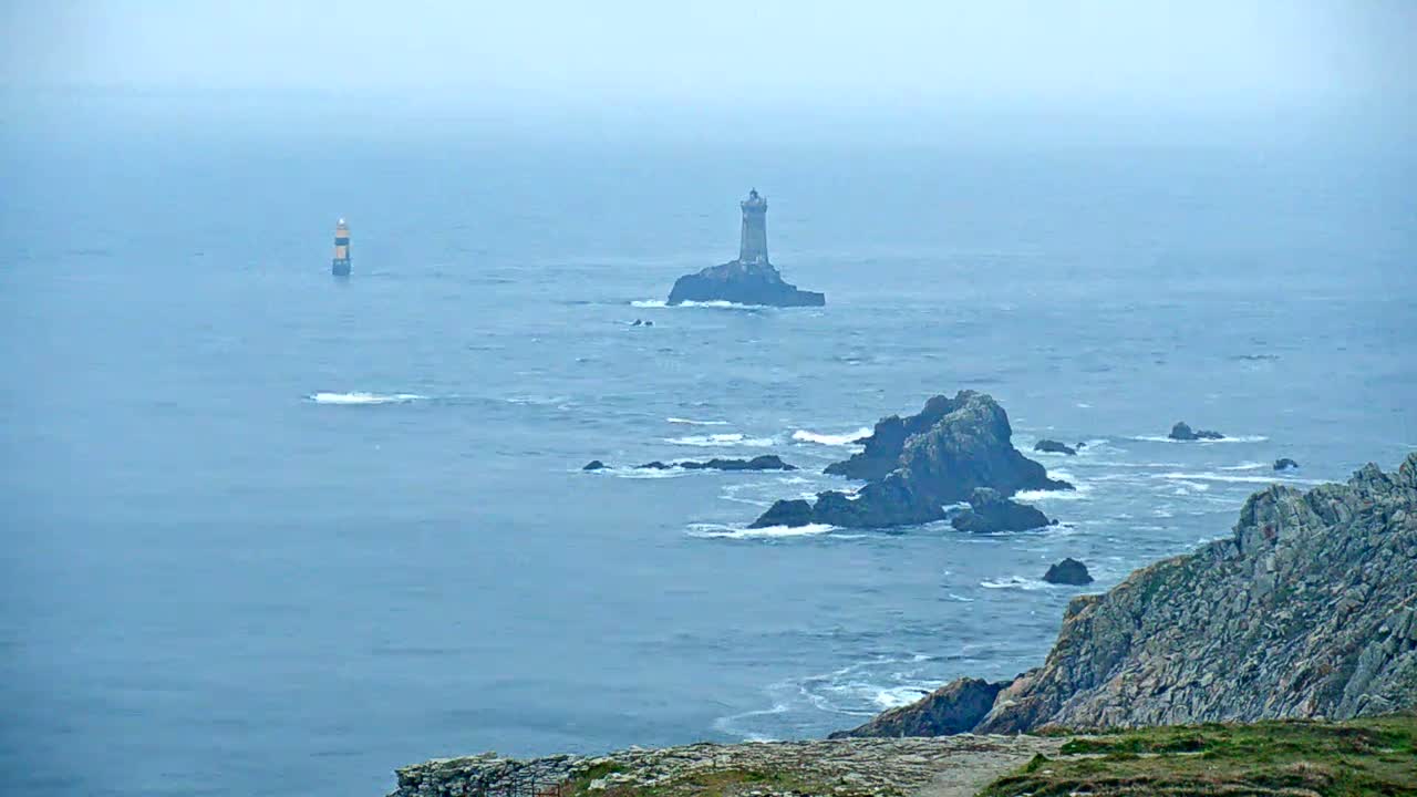 Two lighthouses stand on rocky outcrops in a misty, blue ocean, with a rugged coastline visible in the foreground.