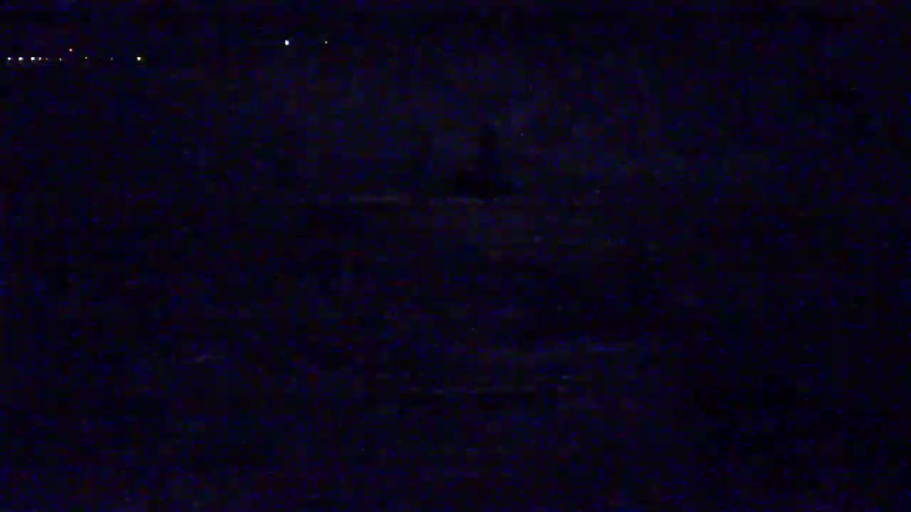 A dark, nighttime scene shows a blurry, indistinct landscape under a clear sky with a few distant lights.