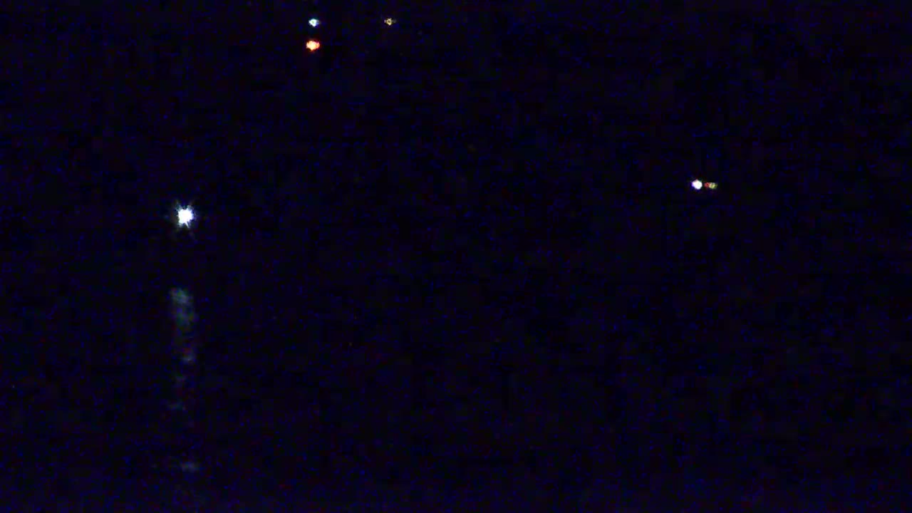 A dark night sky shows several bright lights, including a large, bright light with a faint vertical streak below it.