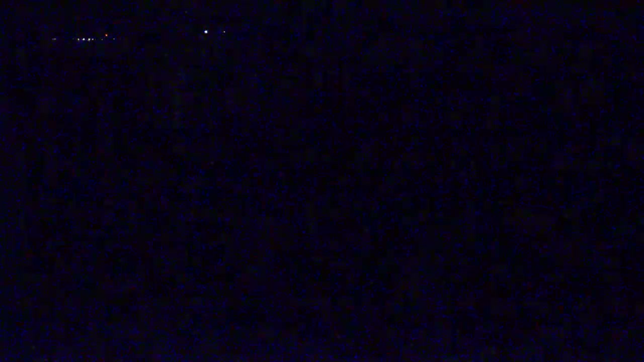 A dark, nighttime scene shows a distant line of faint lights against a very dark background.