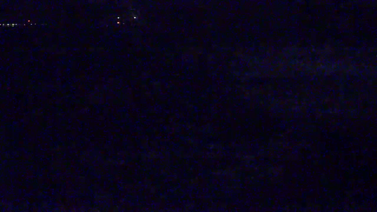 A dark, nighttime scene shows a few faint lights in the distance.
