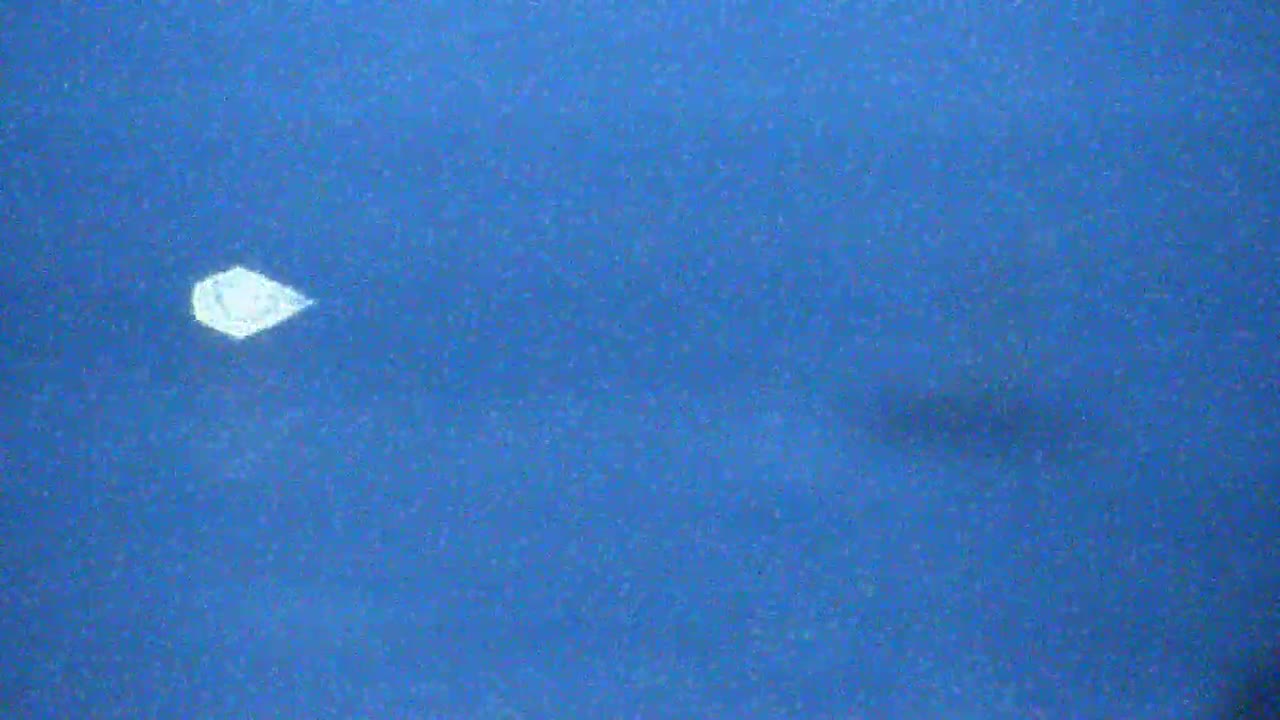 A small, bright white object is visible in a clear, blue sky.