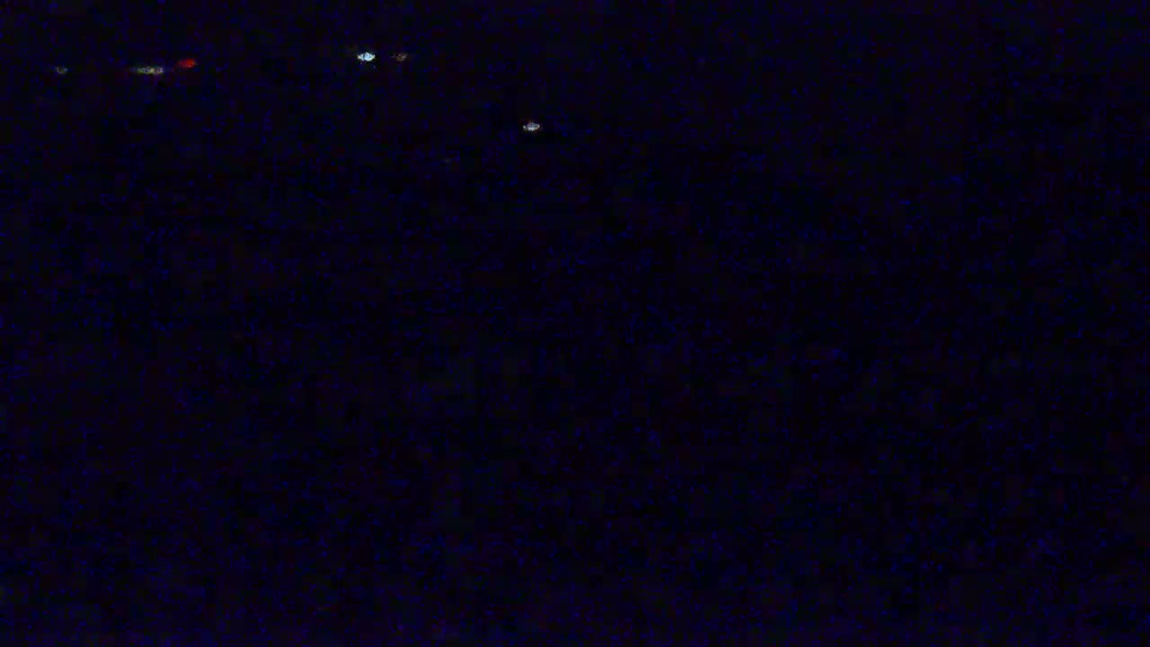 A dark, grainy image shows a few faint lights in the distance at night.