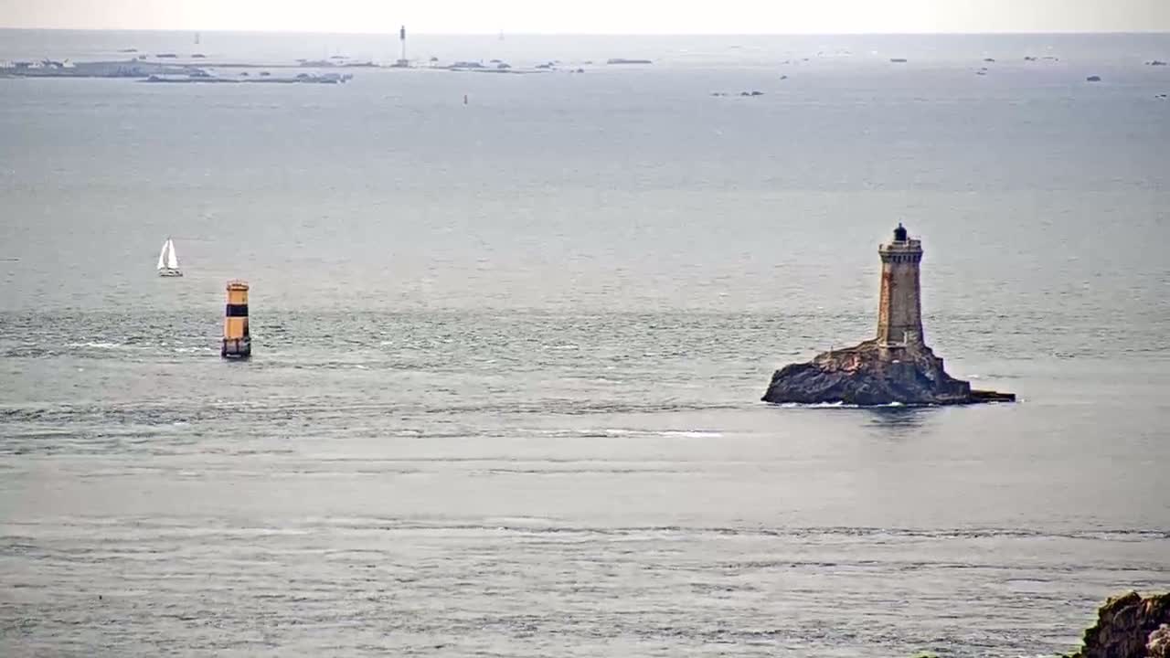 A sailboat and a lighthouse are visible on a calm, gray sea, with land faintly visible in the distance.