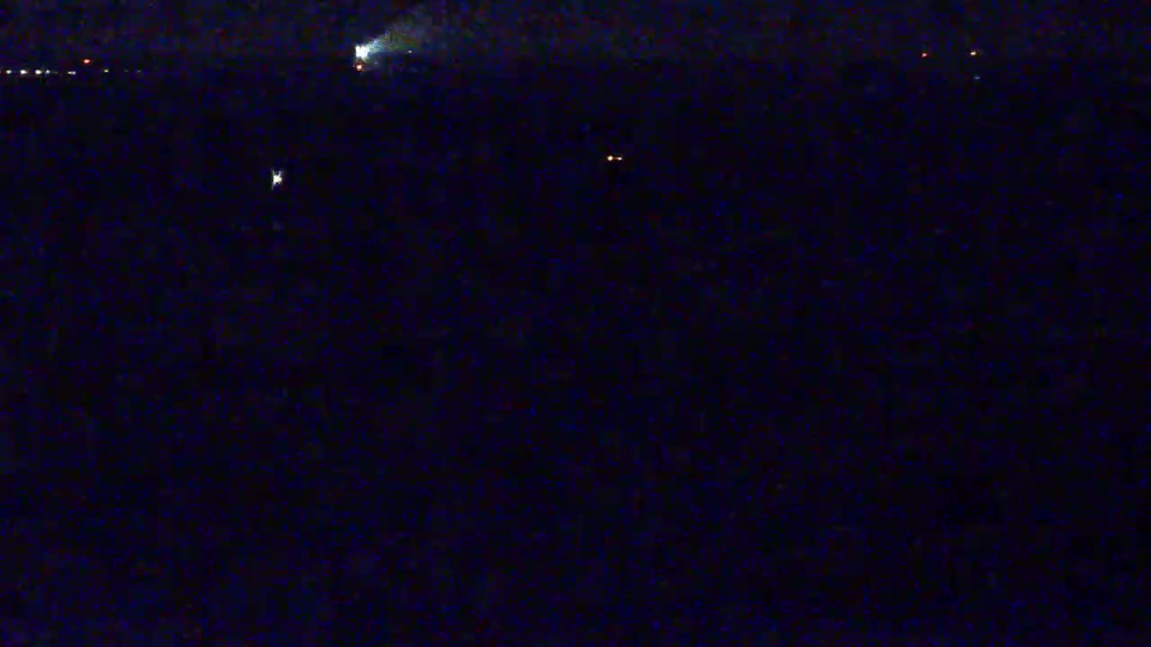 A dark, nighttime scene shows several faint lights in the distance across a dark body of water.