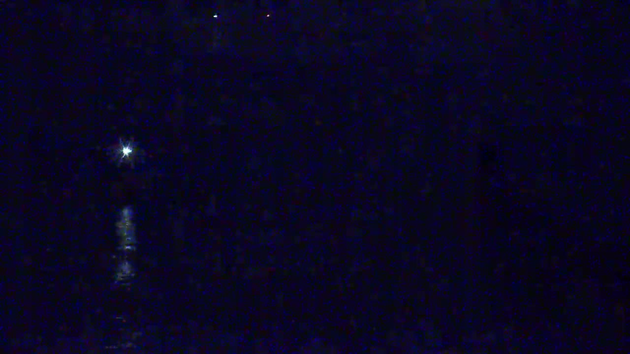 A bright light, possibly a lighthouse, shines over dark water at night.