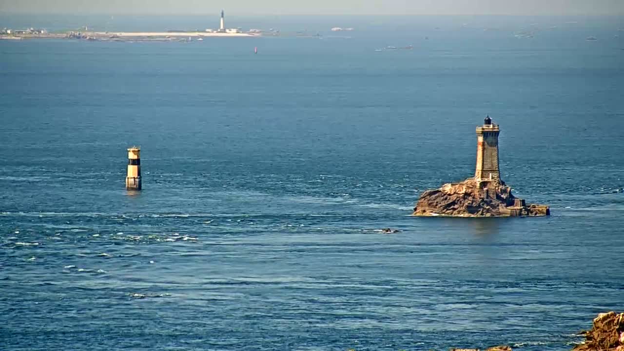 Two lighthouses stand in a calm blue ocean, with a distant landmass visible on the horizon under a clear sky.