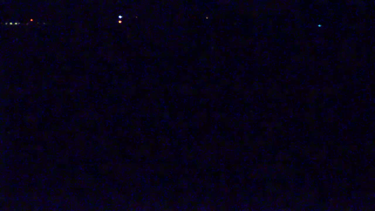 A dark, nighttime scene with a few faint lights visible in the distance.