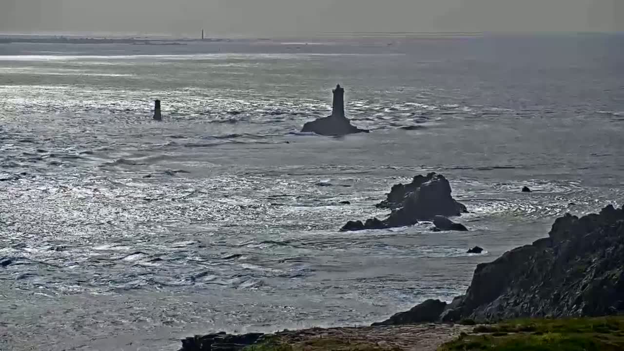 A rocky coastline with two lighthouses is visible on a windy, gray day, with choppy waves breaking against the rocks.