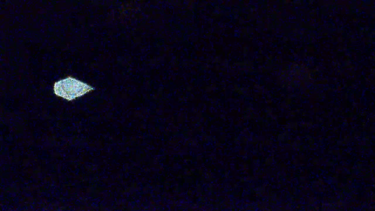 A faintly luminous, oblong object is seen against a dark, nighttime sky.