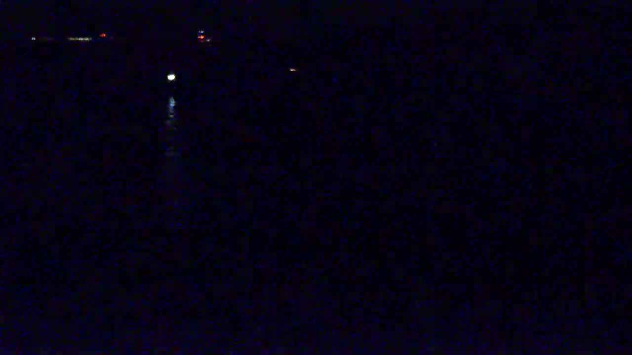 A dark, nighttime scene shows a body of water with several distant lights and a brighter light closer to the camera.