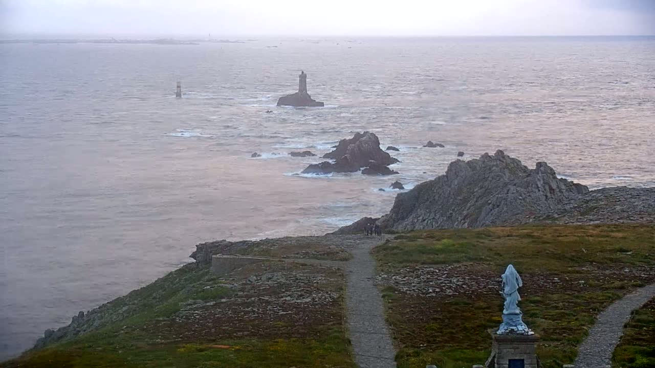 A rocky coastline with a statue and several lighthouses visible in the distance under an overcast sky.