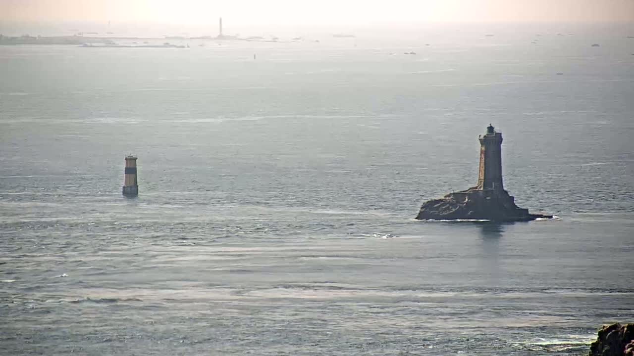 Two lighthouses stand in a calm, hazy ocean, with a distant shoreline visible in the background.