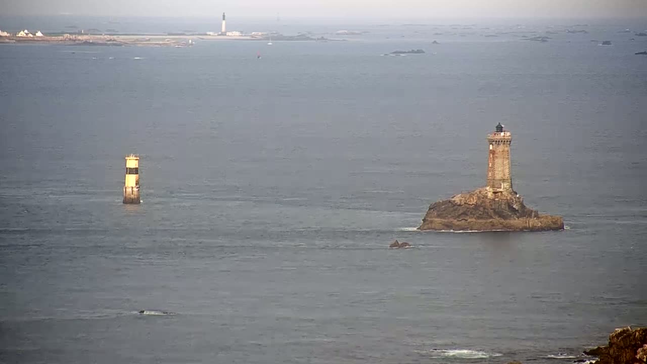 Two lighthouses stand in a calm, gray sea, with a distant landmass visible in the background.