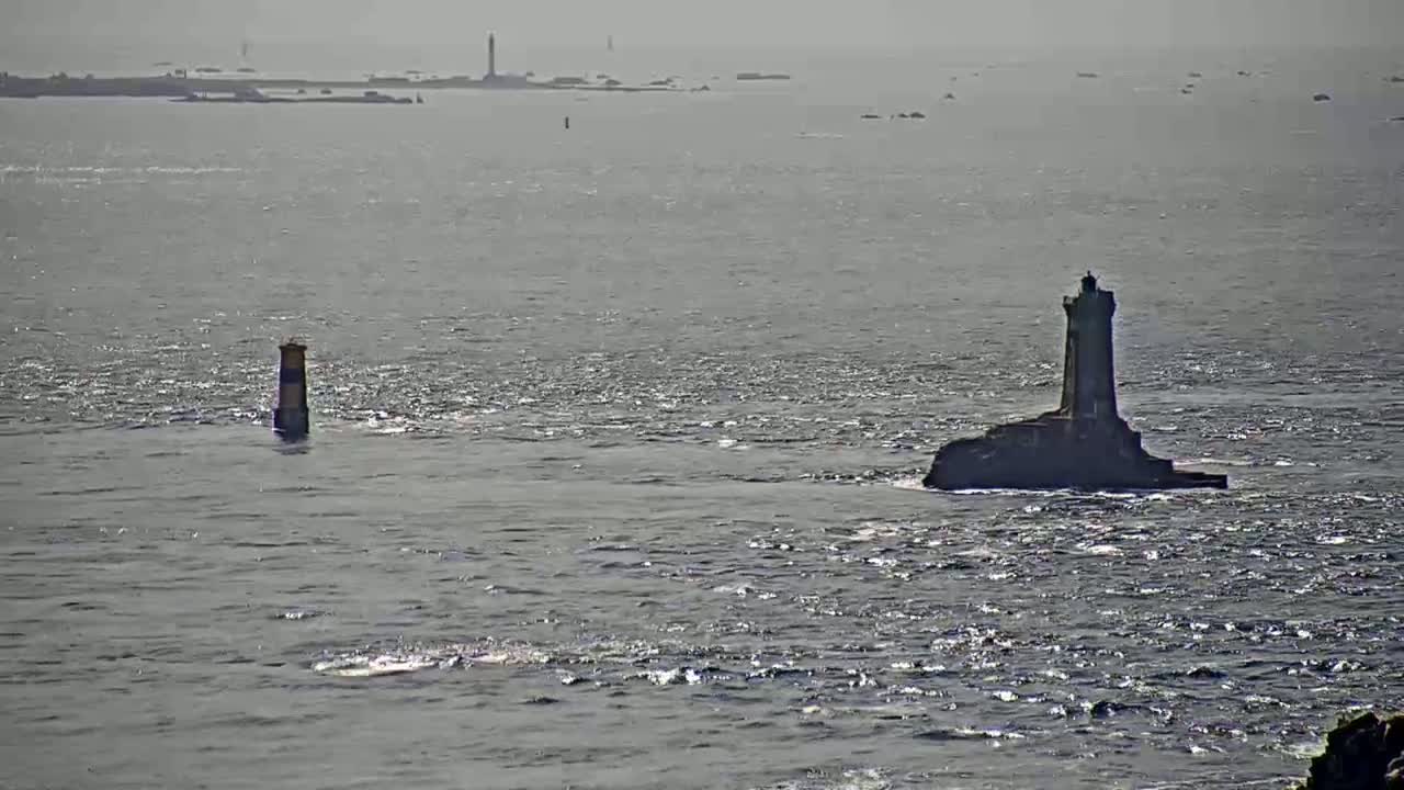 Two lighthouses stand in a calm, gray sea under a hazy sky, with a distant landmass visible in the background.