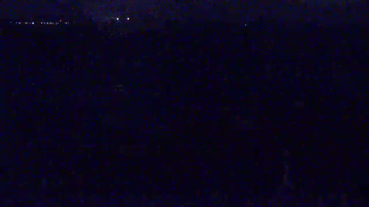 A dark, nighttime scene shows a distant line of lights, possibly a city skyline, against a very dark, possibly overcast sky.