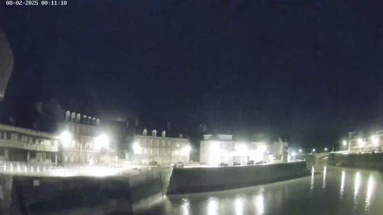 A nighttime view of a calm waterway beside a town with several buildings illuminated by streetlights.