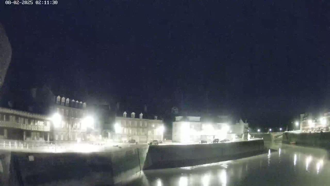 A nighttime view of a calm waterway beside a row of illuminated buildings.