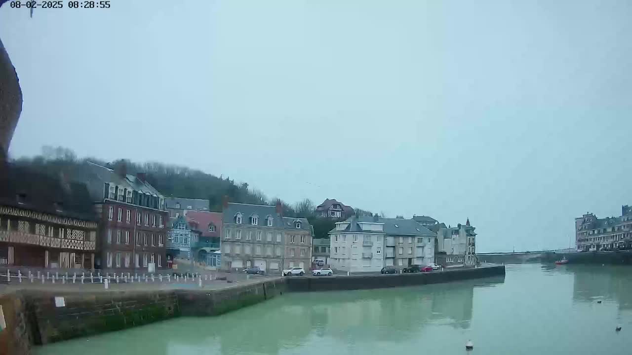 A calm, overcast day reveals a waterfront town with multi-story buildings lining a canal.
