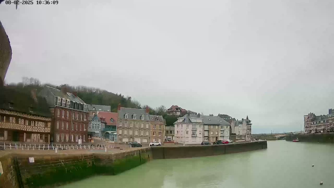 A calm, overcast day reveals a waterfront town with multi-story buildings lining a waterway.