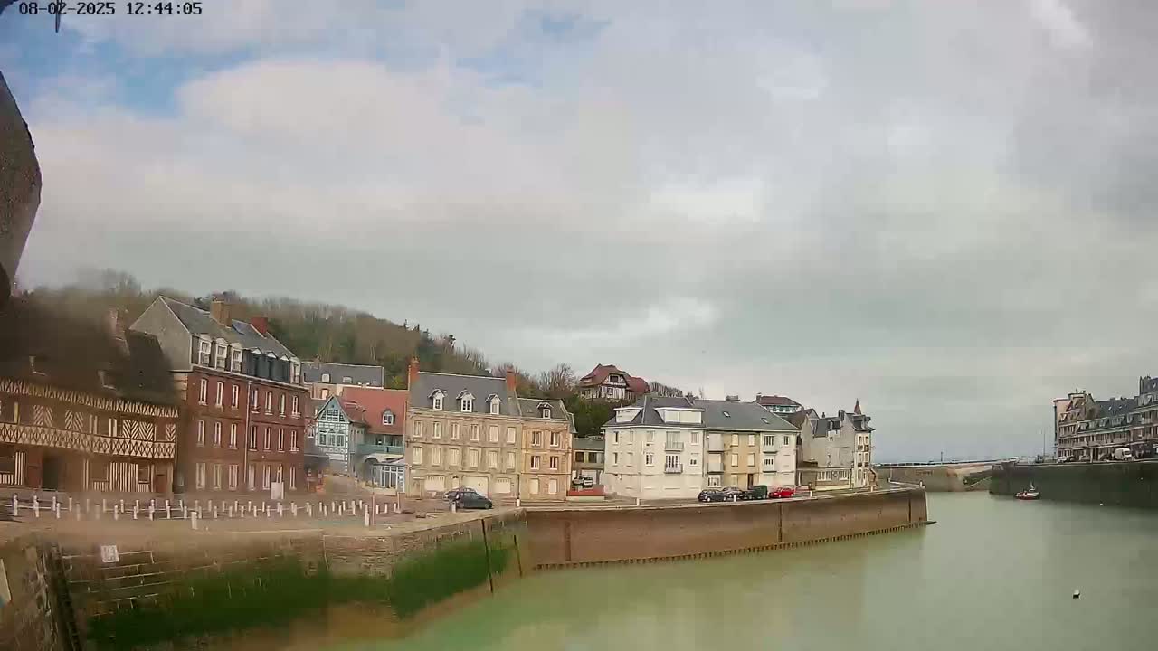 A calm waterway flows between rows of multi-story buildings under a cloudy sky.