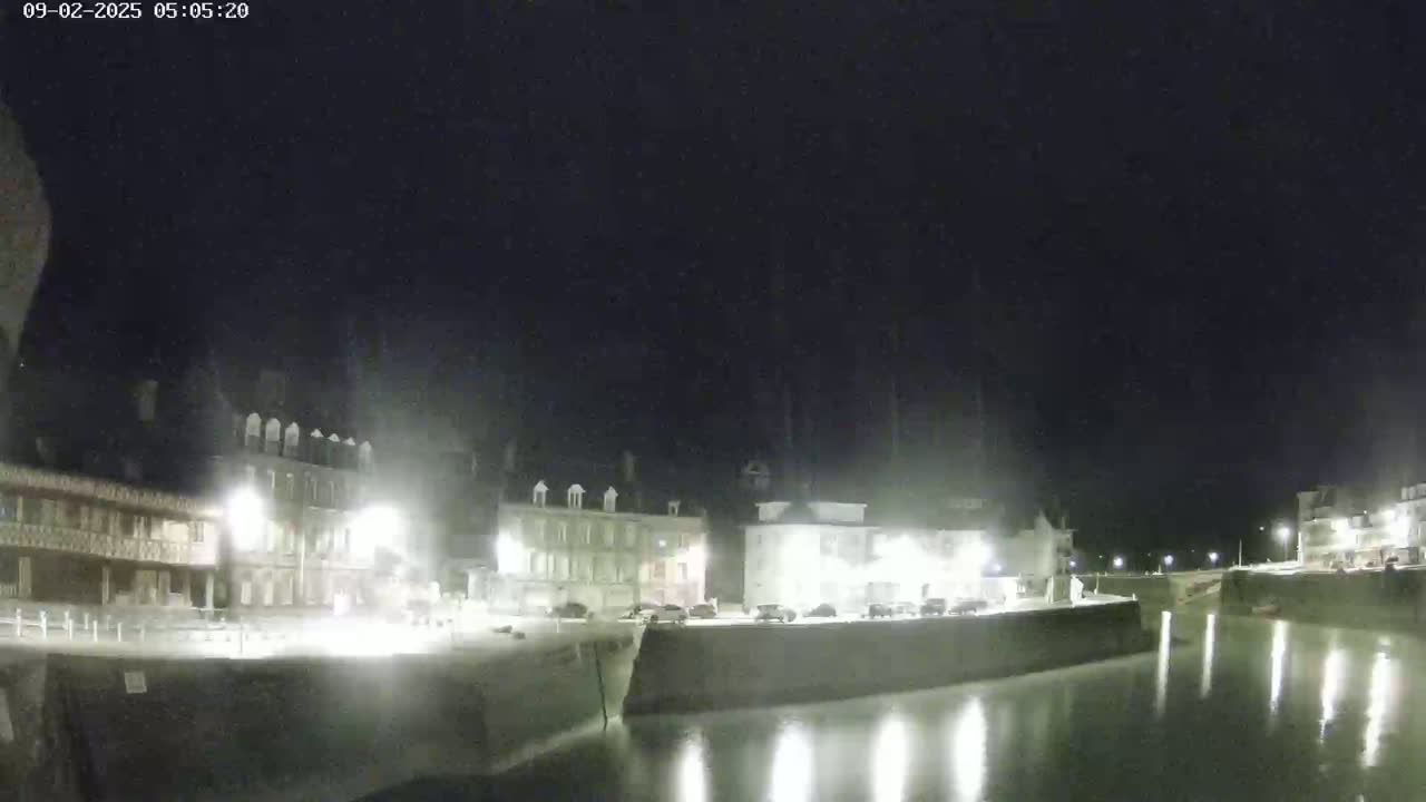 A nighttime view of a calm harbor, lined with buildings illuminated by streetlights.