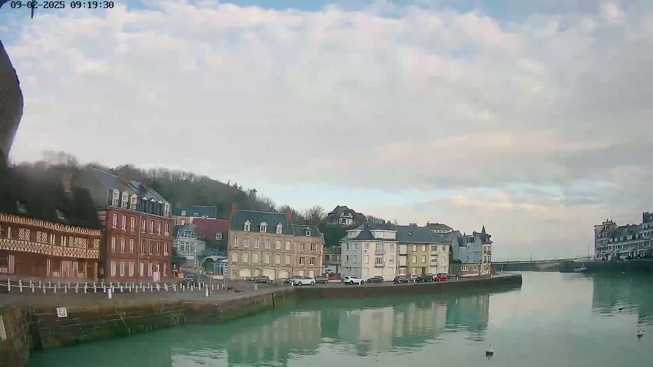 A calm waterway reflects buildings along its banks under a cloudy sky.