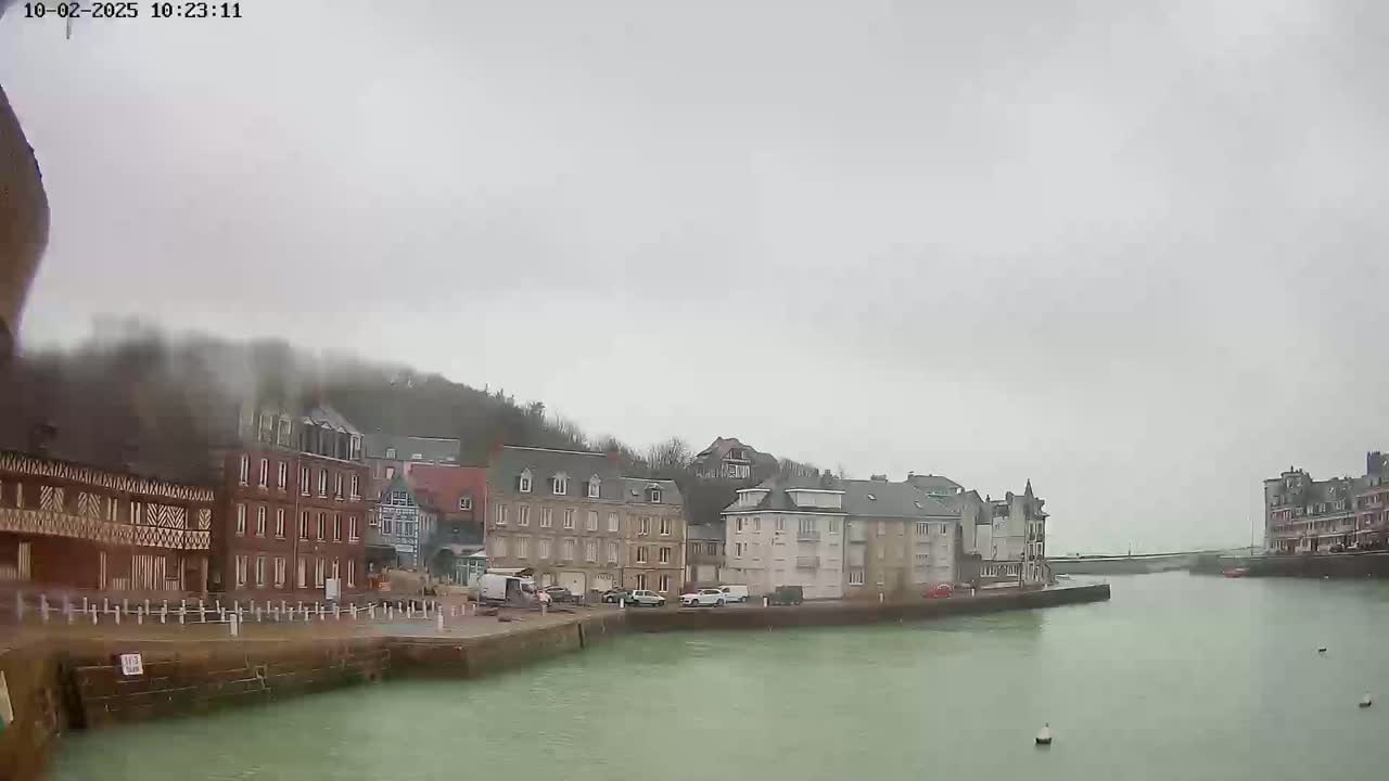 A cloudy day shows a waterfront town with multi-story buildings lining a calm waterway.