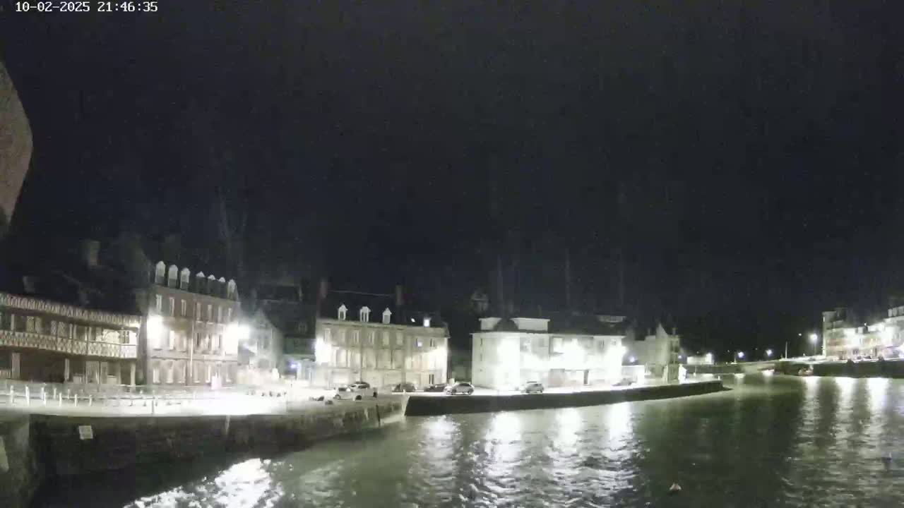 A nighttime view of a calm waterway reflecting the lights of buildings lining its banks under a dark sky.