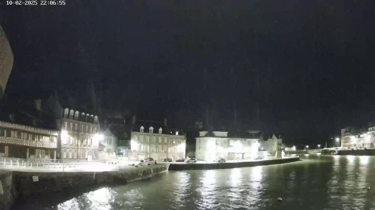 A nighttime view of a calm body of water beside a waterfront town with several buildings lit up.