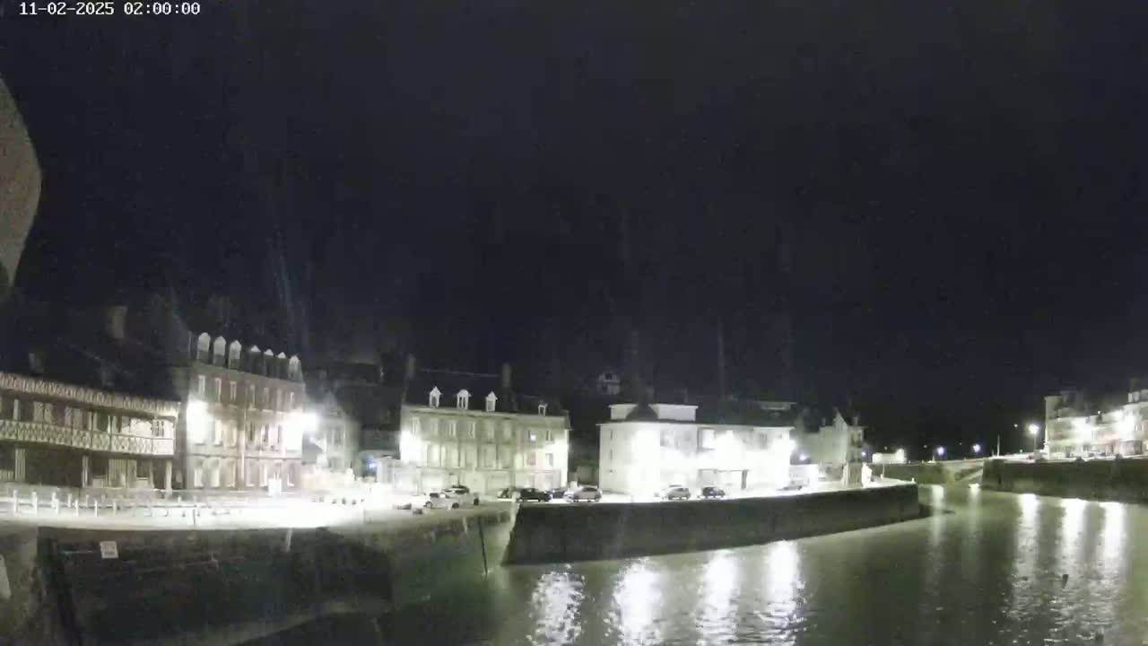 A nighttime view of a calm canal reflecting lights from buildings along its banks under a dark sky.