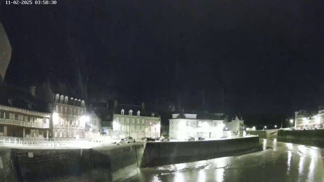 A nighttime view of a waterfront town with several buildings lit along a calm, shallow waterway under a dark sky.
