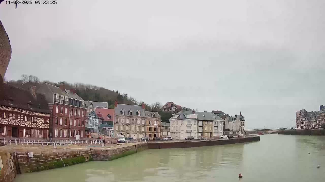 A calm, overcast day reveals a waterfront town with several multi-story buildings lining a canal.