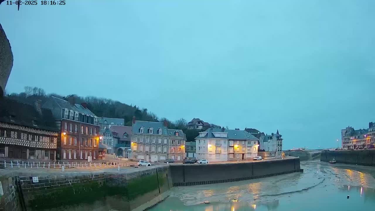 Under a twilight sky, a waterfront town with multi-story buildings lines a narrow waterway at low tide.