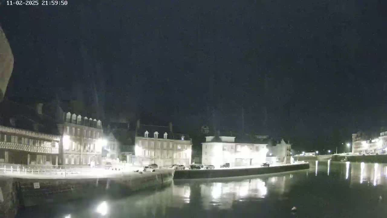 A nighttime view of a calm canal reflecting the lights of buildings along its banks under a clear, dark sky.
