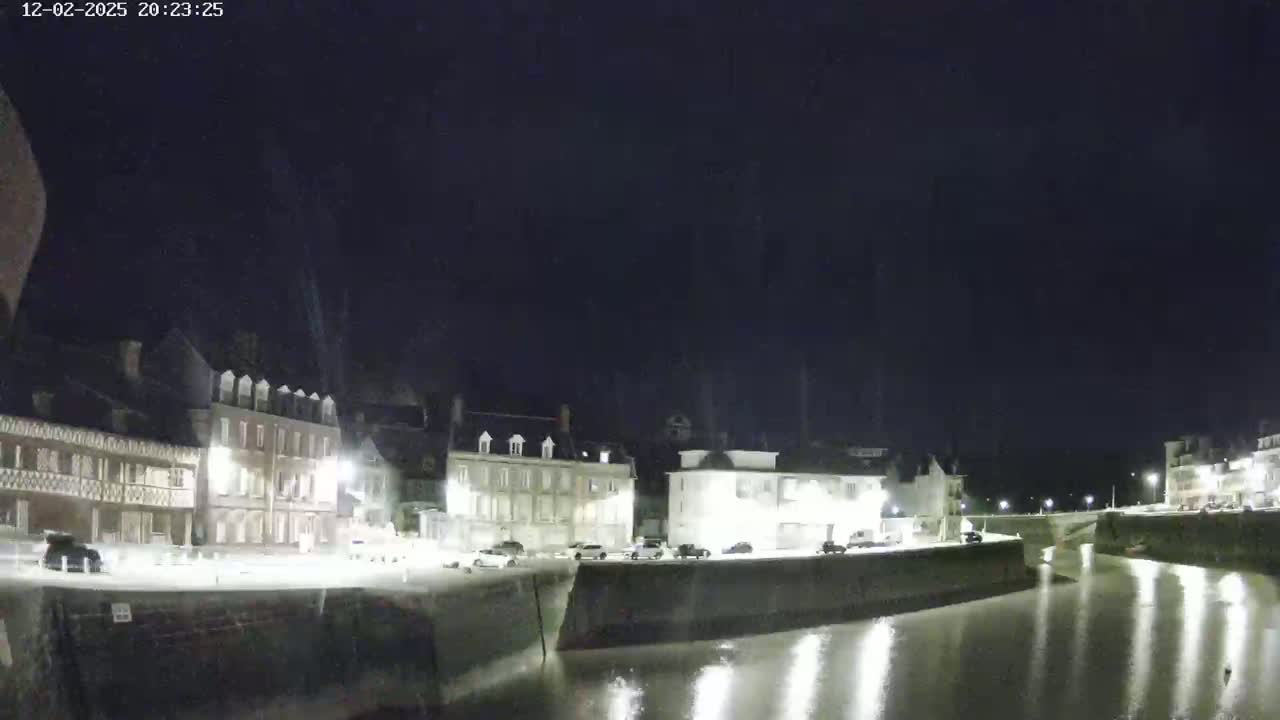 A nighttime view of a calm waterway beside a row of buildings illuminated by streetlights.