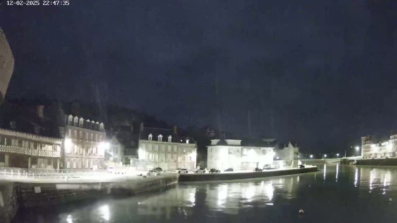 A nighttime view of a waterfront town with several buildings lining a calm canal under a dark, clear sky.