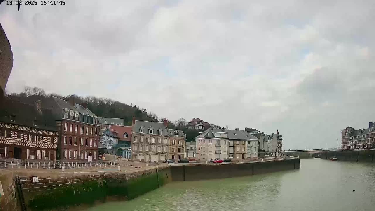 A calm waterway separates rows of multi-story buildings under an overcast sky.