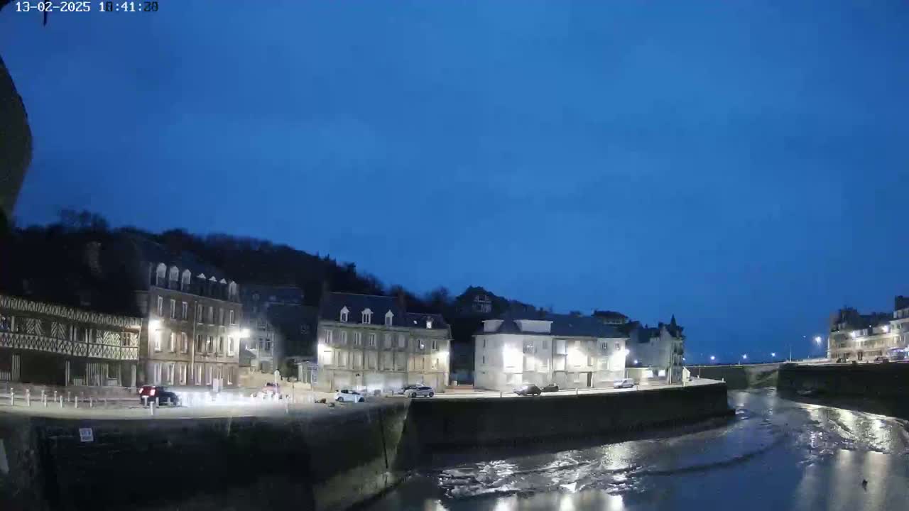 A waterfront town at twilight, with a calm body of water reflecting the lights from buildings lining the shore.