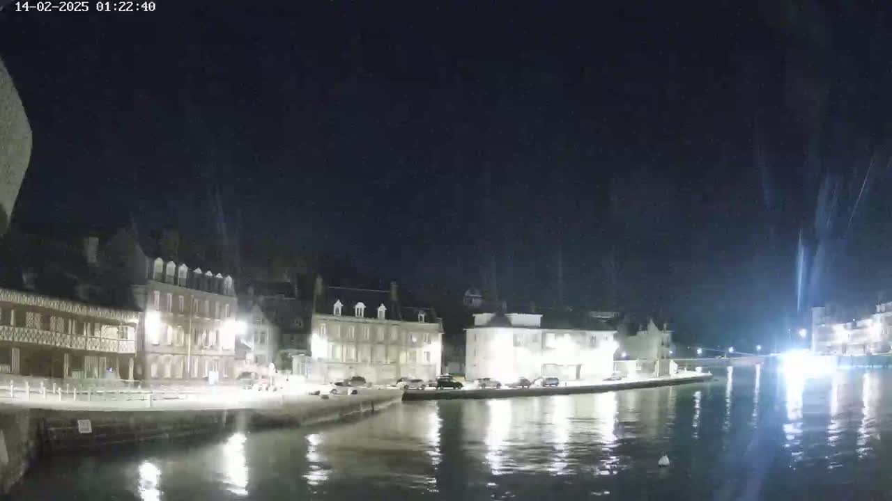 A nighttime view of a calm waterway reflecting the lights of buildings along its banks under a dark, clear sky.