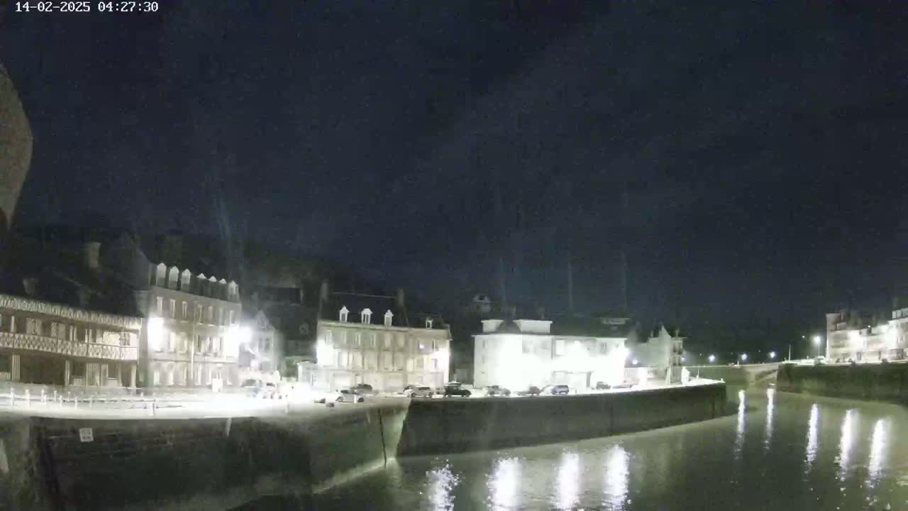 A nighttime view of a calm waterway beside a row of buildings under a dark, clear sky.
